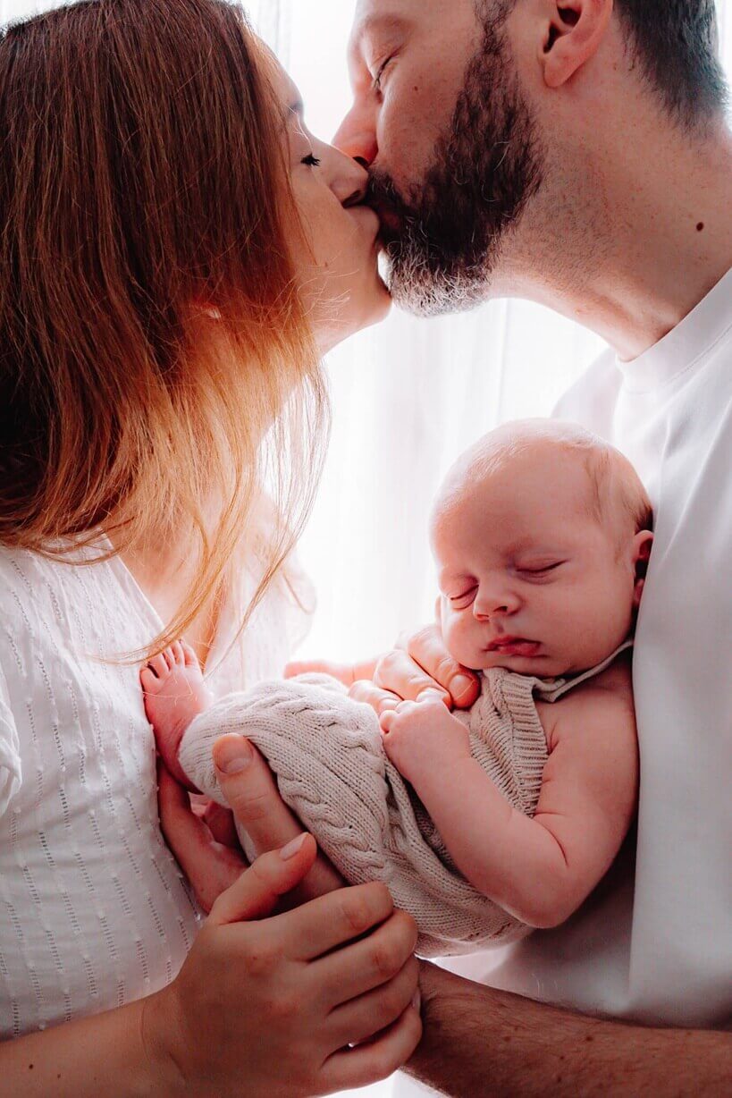 neugeborenenfotoshooting-eltern-kuss-baby-schlaeft