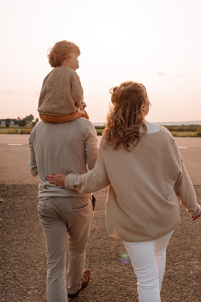 Familienshooting bei Sonnenuntergang – Eltern spazieren mit ihrem Kind