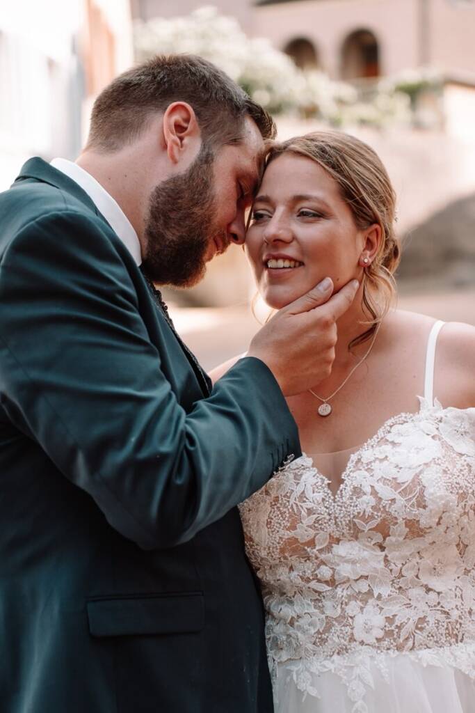 Bräutigam hält liebevoll das Kinn seiner lächelnden Braut, während sie Stirn an Stirn im warmen Licht stehen.